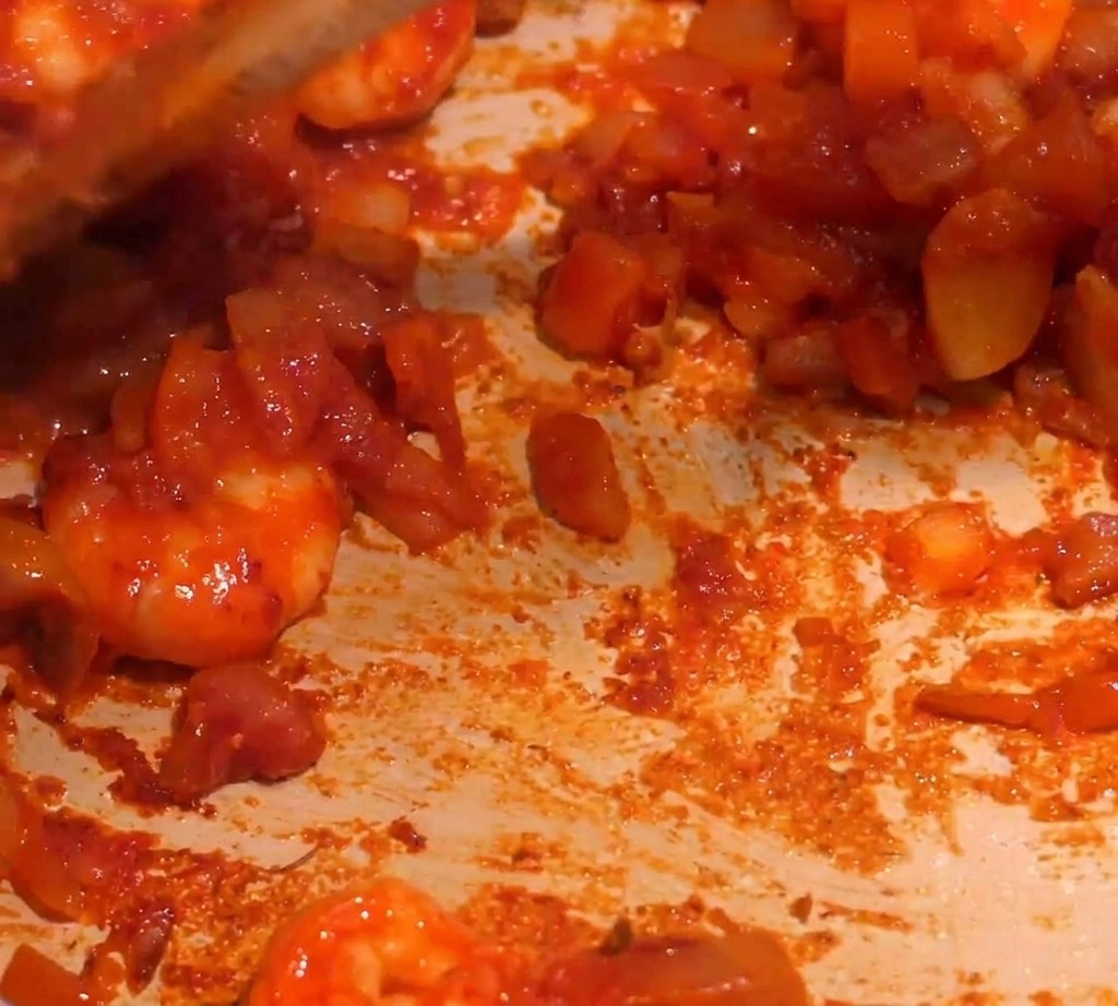 Una densa salsa rossa ai gamberi mescolata in padella mentre viene aggiunto del liquido per farla sobbollire.