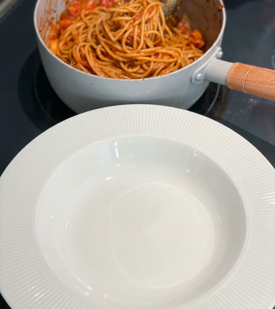 Una pentola di pasta ai gamberi piccante accanto a una ciotola bianca pronta sul piano cottura.