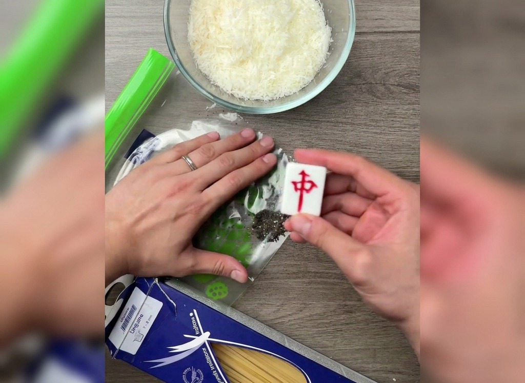 Una mano che utilizza il lato piatto di una tessera pesante per schiacciare i grani di pepe nero allinterno di un sacchetto di plastica.