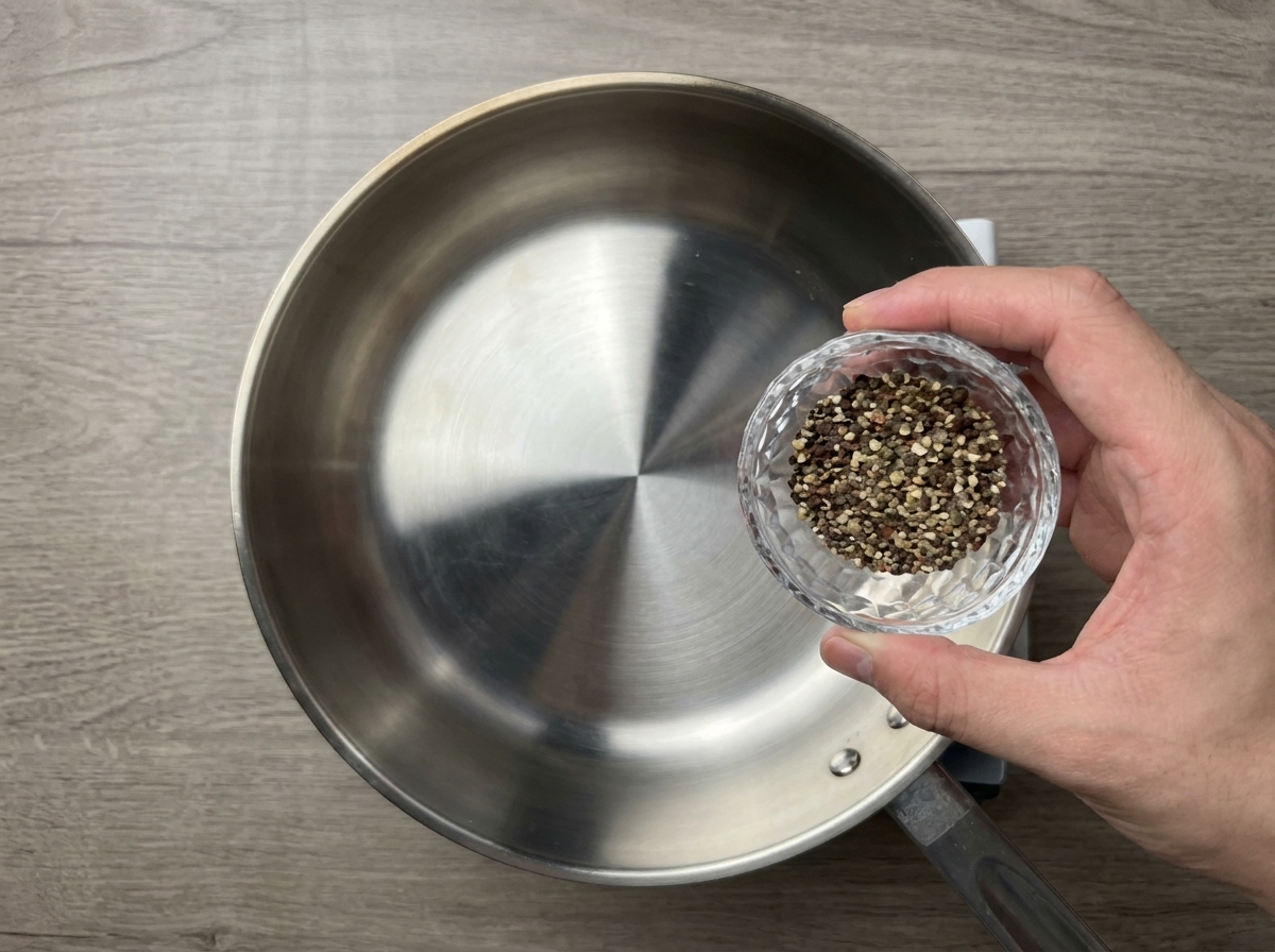 Pepe nero pestato grossolanamente versato da una ciotolina in una padella di acciaio inox già scaldata.