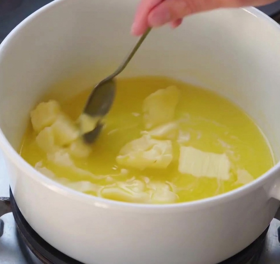 Una frusta che mescola una salsa bianca e liscia mentre si addensa in una pentola bianca sul fuoco.