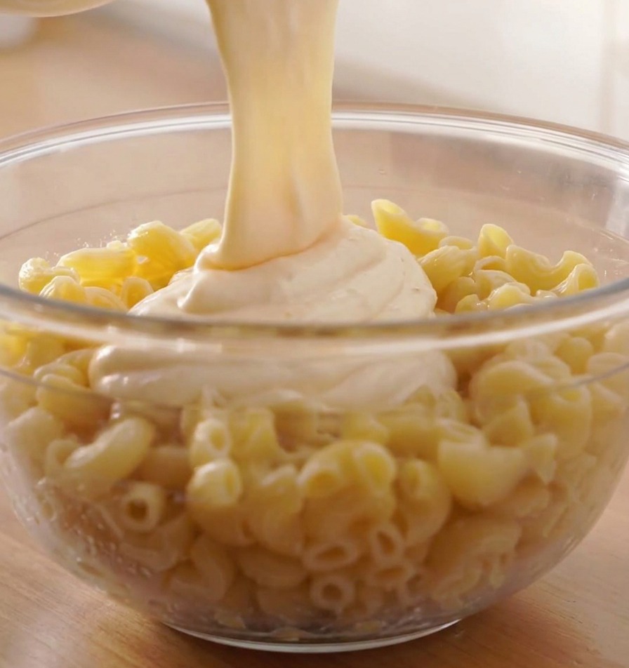 Un abbondante flusso di salsa al formaggio bianca fusa versata sopra unampia ciotola di fusilli cotti.