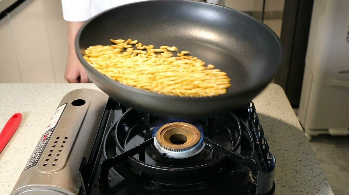 Pinoli che saltano in una padella antiaderente nera su una fiamma a gas blu.