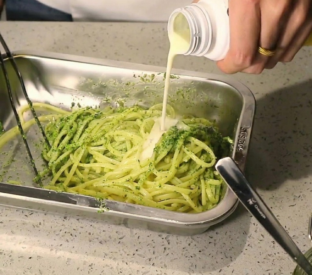 Un filo di crema bianca versata sulla pasta già condita con il pesto verde.