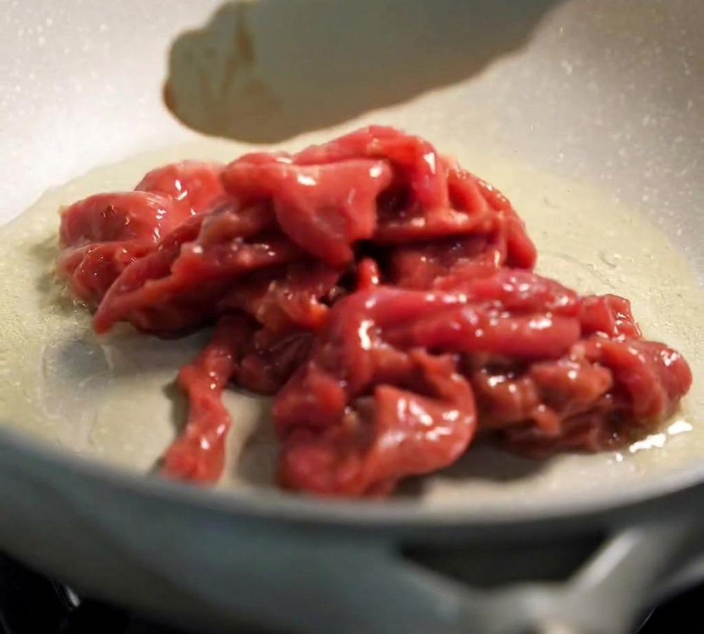 Pinze da cucina che adagiano il manzo marinato in una padella calda e oliata.