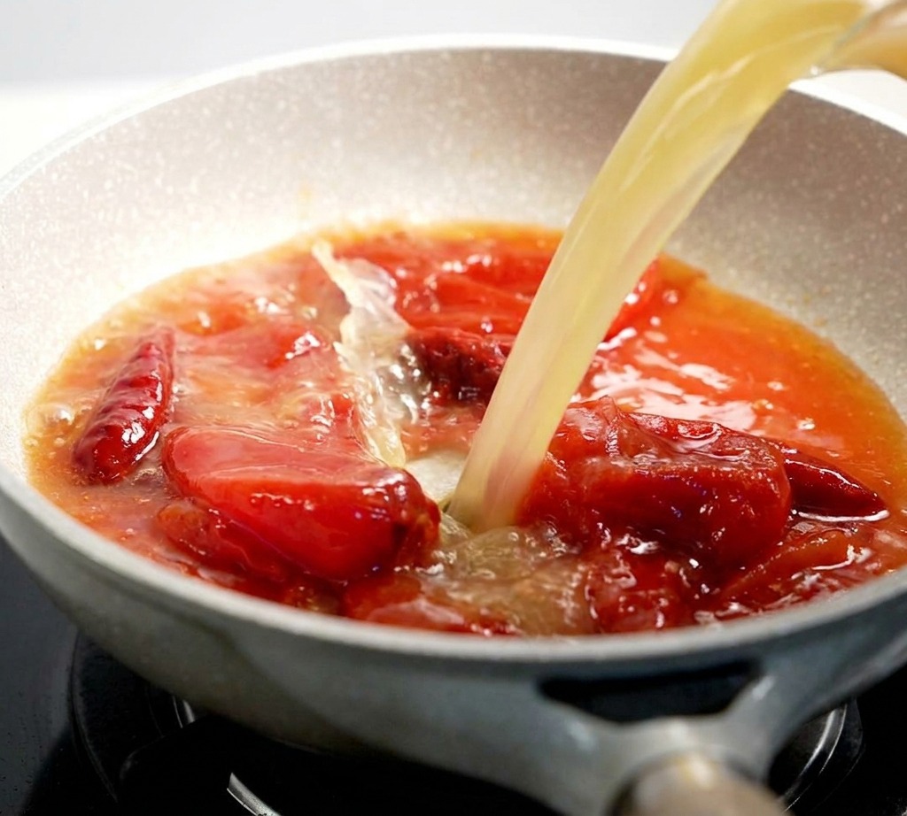 Brodo chiaro versato in una padella con una salsa di pomodoro rossa che bolle.