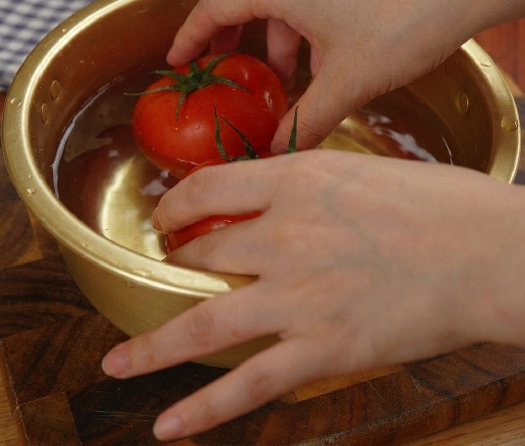 Due pomodori rossi surgelati immersi in una ciotola di metallo dorata piena dacqua.