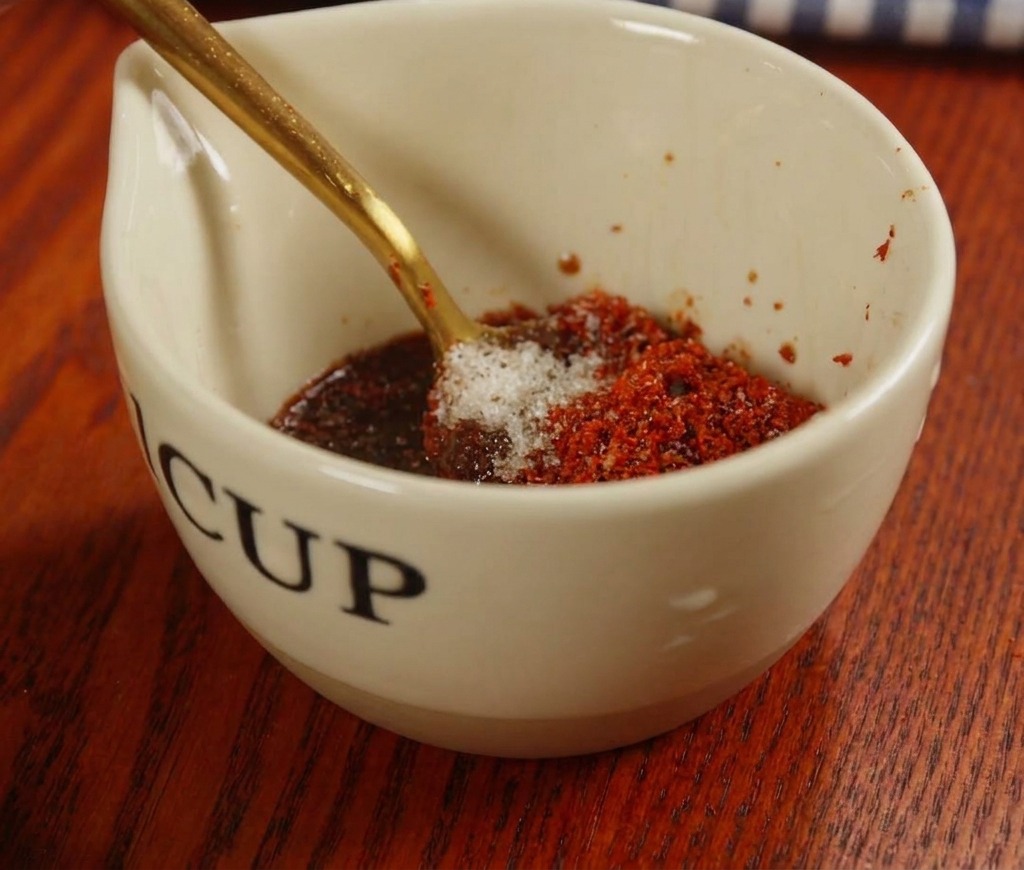 Miscela di una salsa rossa con pasta di peperoncino e spezie in una tazzina di ceramica con un cucchiaio dorato.