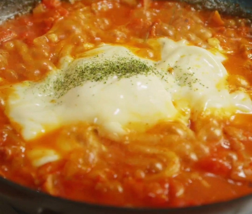 Erbe verdi essiccate spolverate sopra uno strato di formaggio fuso bianco e giallo sui noodle.
