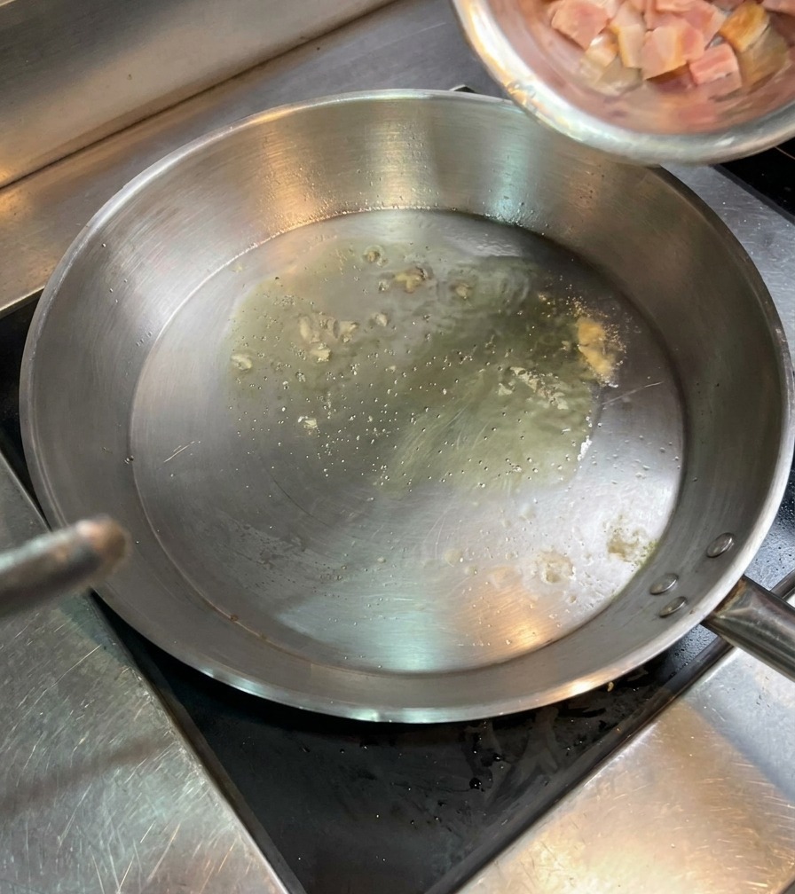 Cubetti di bacon crudo versati da una ciotola in una padella con olio bollente.