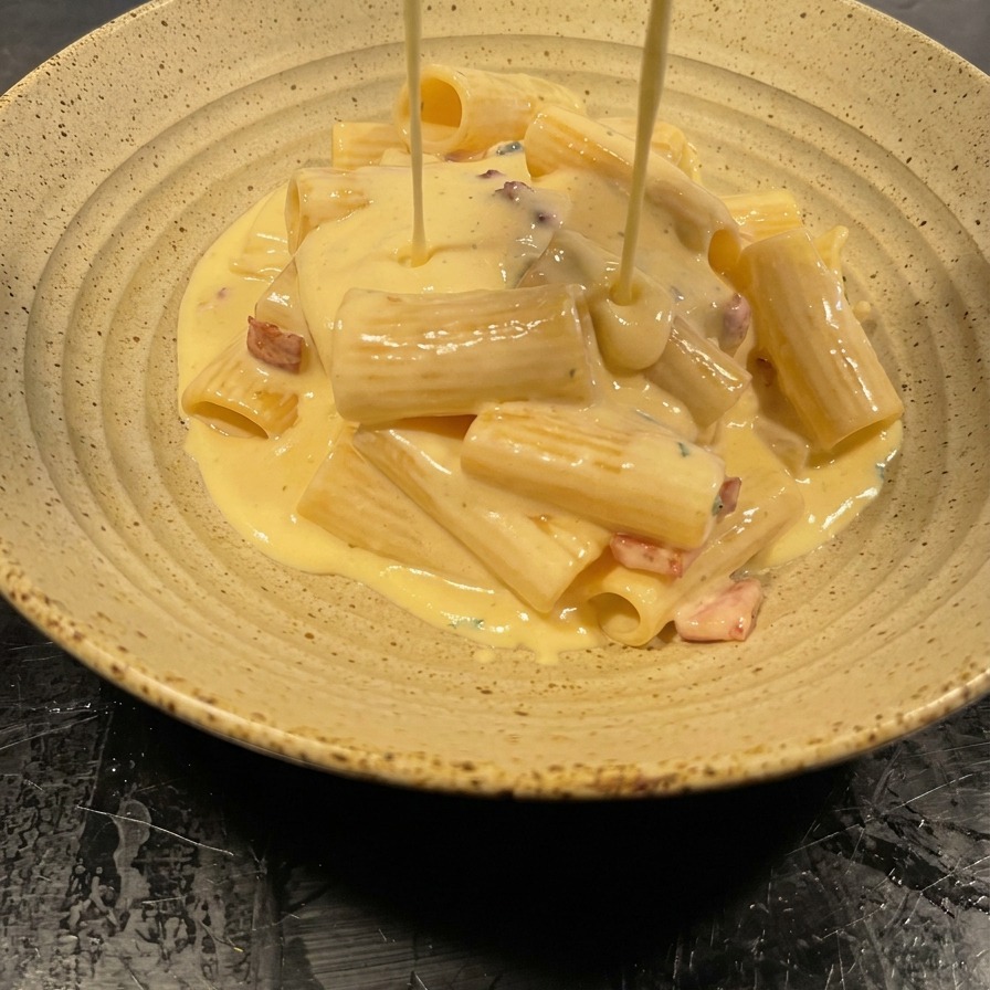 Salsa vellutata versata dalla padella sopra una montagna di rigatoni in una ciotola.