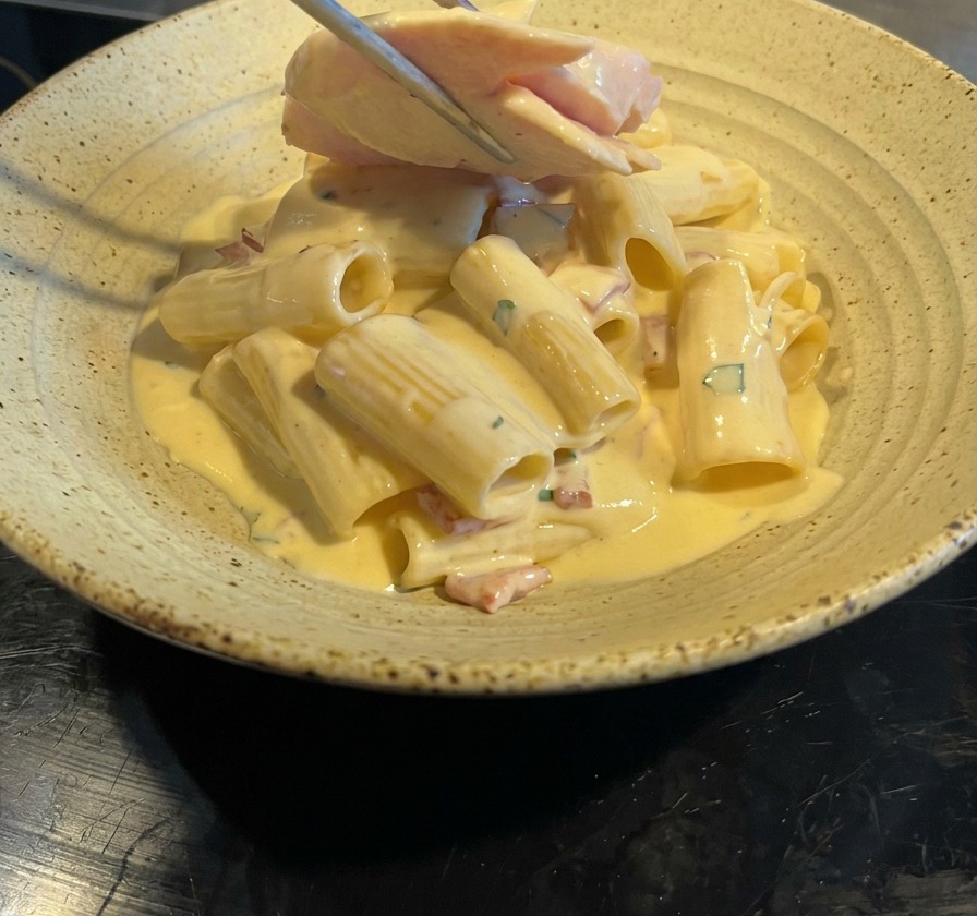 Pinze di metallo che posizionano fette di pollo scottato sopra i rigatoni cremosi.