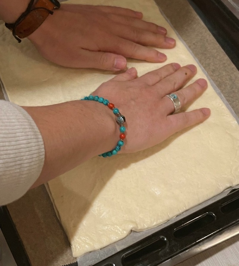 Una persona che stende una base rettangolare per pizza su una teglia nera foderata con carta forno.