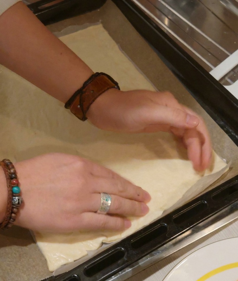 Due mani che premono su una base rettangolare per pizza per appiattirla e definire i bordi della crosta.