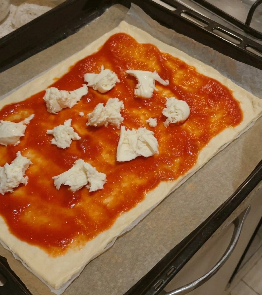 Grossi pezzi di mozzarella bianca fresca posizionati sopra la salsa di pomodoro su una base per pizza.