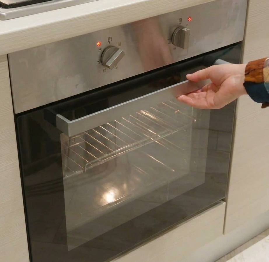 Primo piano di una mano che regola le manopole dargento di un forno in acciaio inox per impostare calore e tempo.
