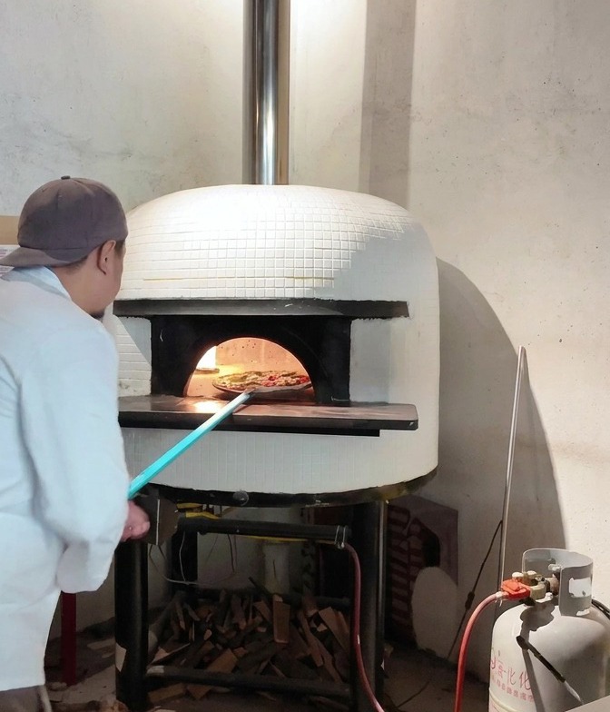 Una pizza Margherita che viene fatta scivolare da una pala nel cuore di un forno a legna ardente.