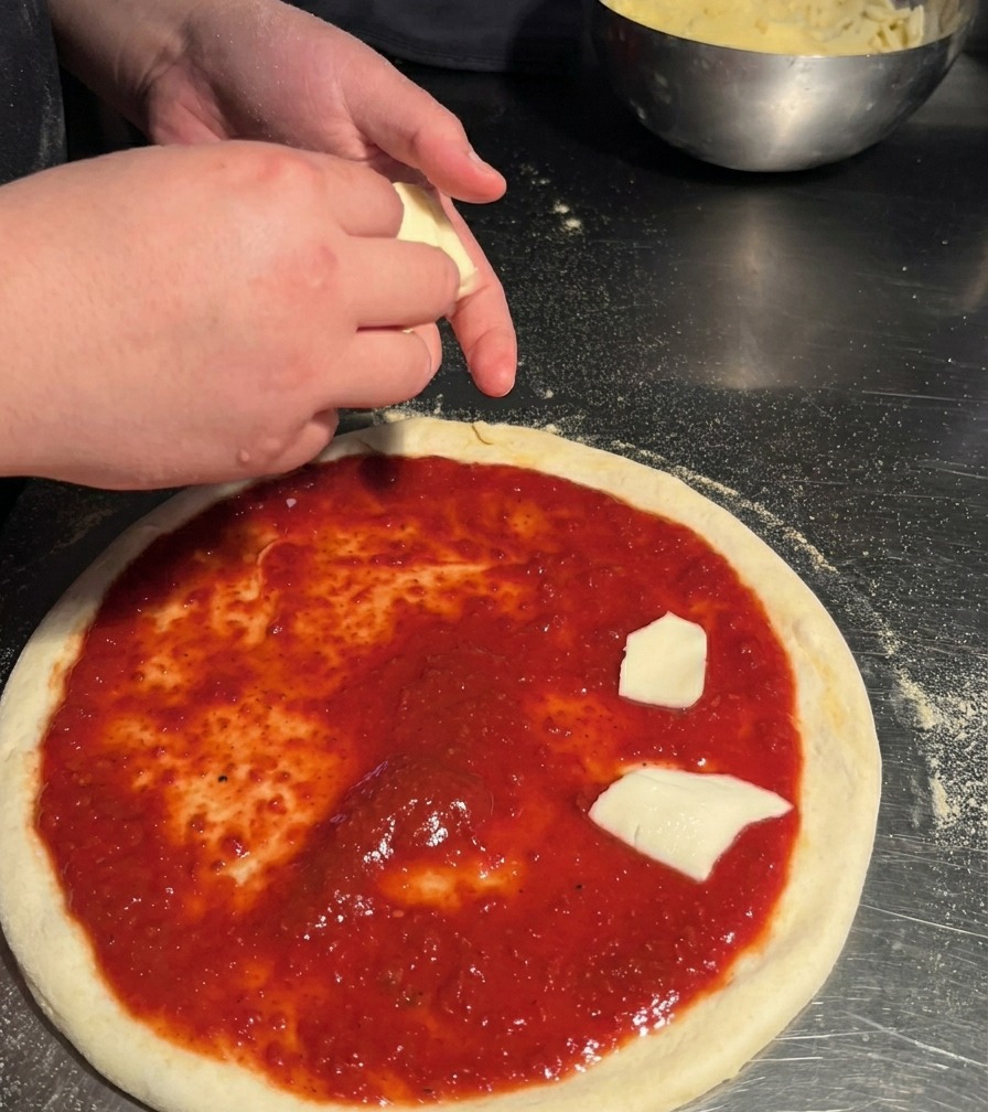 Una persona che distribuisce pezzi di mozzarella bianca tagliati a mano su una base per pizza condita con salsa rossa.