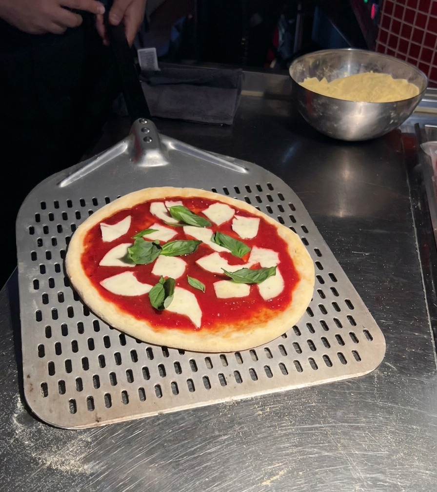 Una pizza Margherita cruda su una pala metallica forata, pronta per essere infornata.