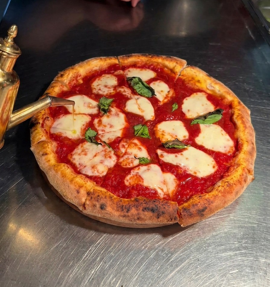 Olio extravergine doliva versato da unoliera su una pizza Margherita a fette.