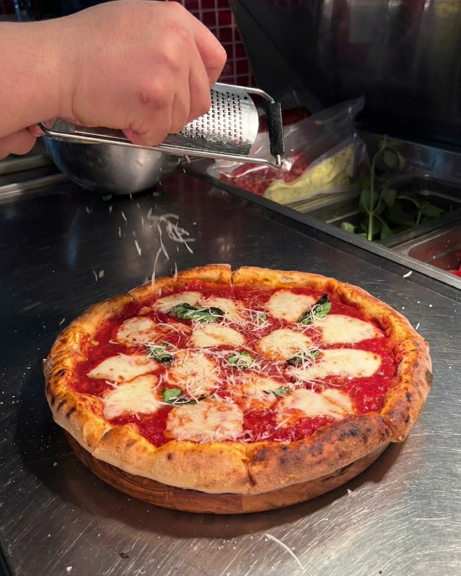Mano che usa una grattugia microplane per grattugiare parmigiano fresco su una pizza napoletana.