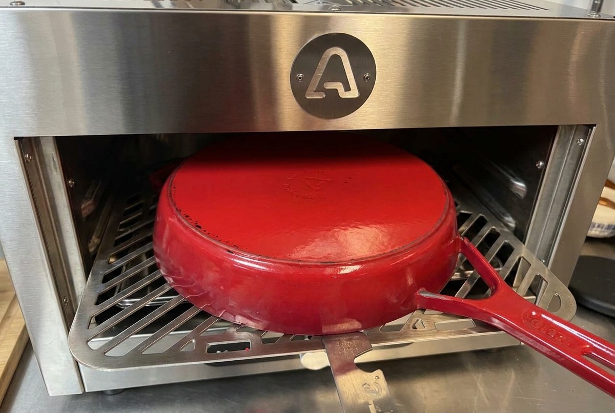 Una pentola in ghisa rossa smaltata posizionata capovolta sulla griglia metallica allinterno di un forno.
