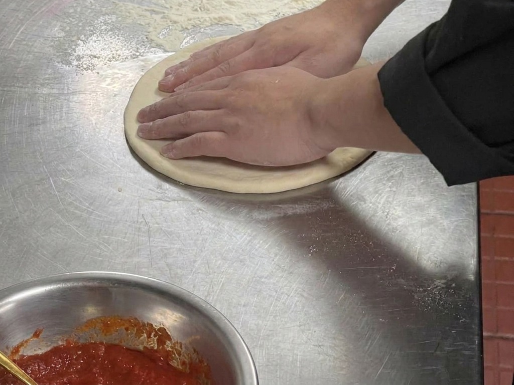 Dettaglio di mani che premono sul bordo di un disco di pasta piatto per creare un bordo esterno rialzato.