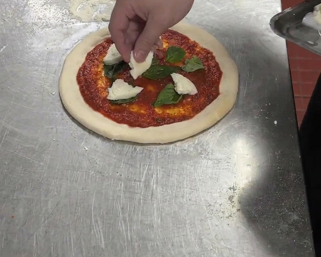 Pezzi di mozzarella di bufala bianca aggiunti a una pizza già condita con salsa di pomodoro e basilico.