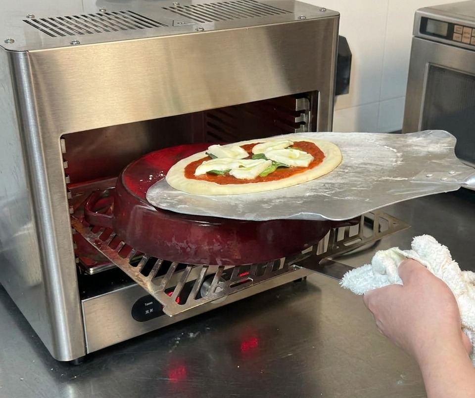 Una pala da pizza in metallo che fa scivolare la pizza cruda sulla pentola in ghisa rovente allinterno del forno.