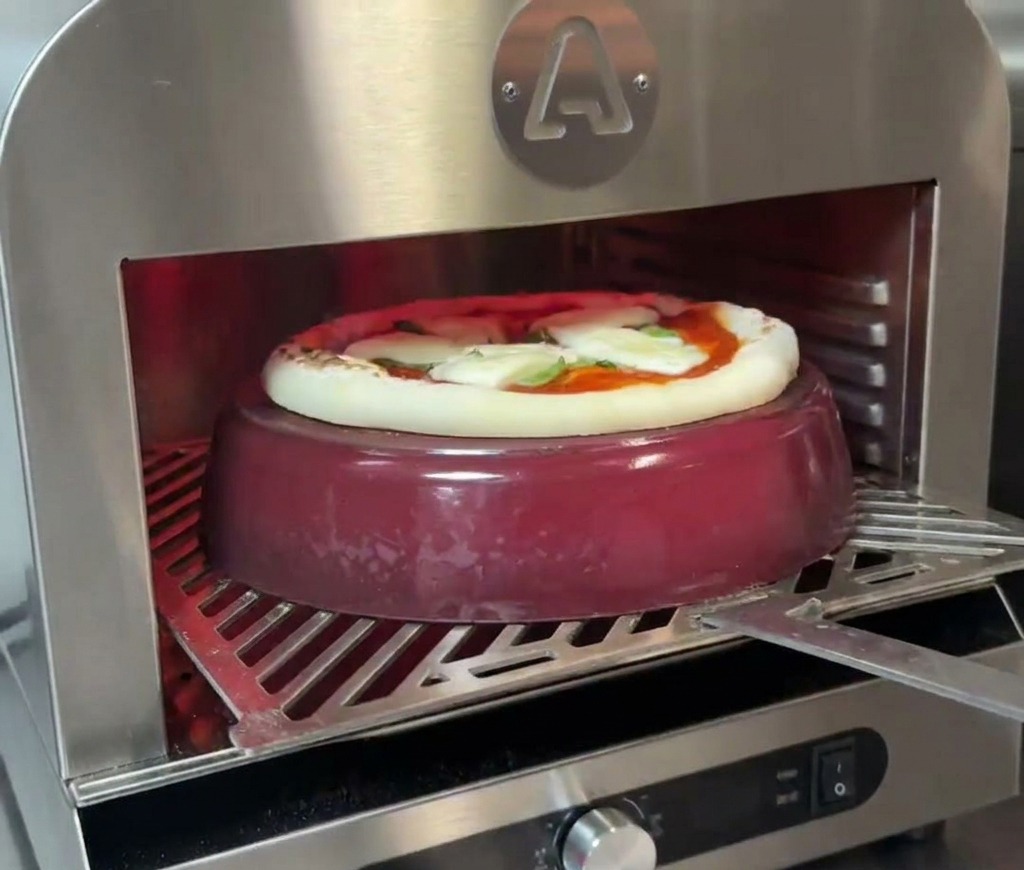Pizza in cottura sopra una pentola di ghisa rossa nel forno, con il cornicione che inizia visibilmente a gonfiarsi e scurirsi.