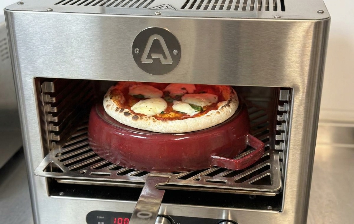Una pala da pizza inserita nel forno per ruotare una pizza quasi cotta sopra la pentola di ghisa.