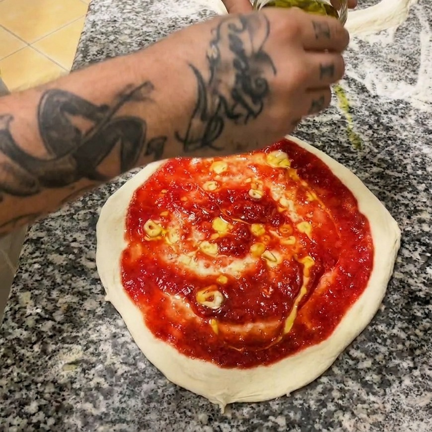 Una mano che usa un cucchiaio di metallo per stendere la salsa di pomodoro rosso vivo con un movimento a spirale.