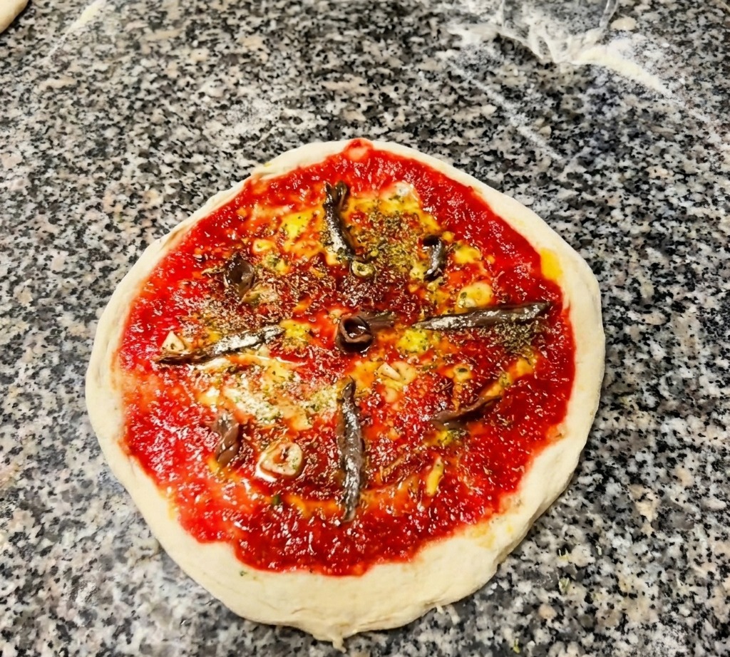 Inquadratura dallalto di una pizza cruda con pomodoro e filetti di acciughe disposti a raggiera.