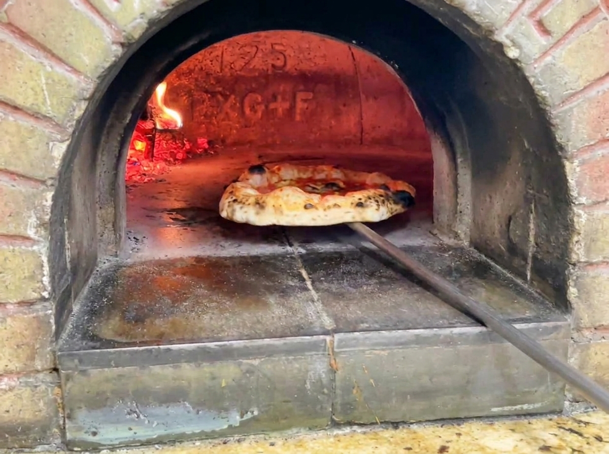 La pizza finita estratta dal forno, con cornicione dorato e macchie scure di bruciatura.