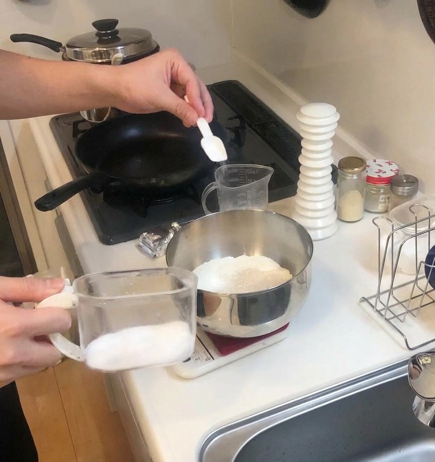 Un piccolo misurino bianco aggiunge sale in una ciotola di farina e lievito su una bilancia da cucina.