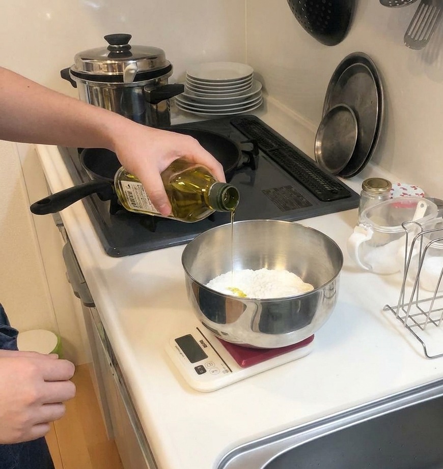 Un filo di olio doliva giallo versato da una bottiglia di vetro in una ciotola con farina.