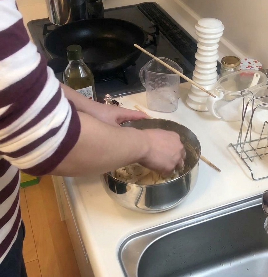 Mani che impastano la pasta per pizza in una ciotola di acciaio su un bancone bianco vicino a una bottiglia dolio.