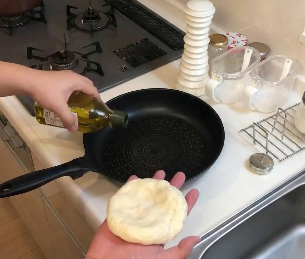 Olio doliva versato da una bottiglia di vetro in una padella antiaderente nera sul fornello.