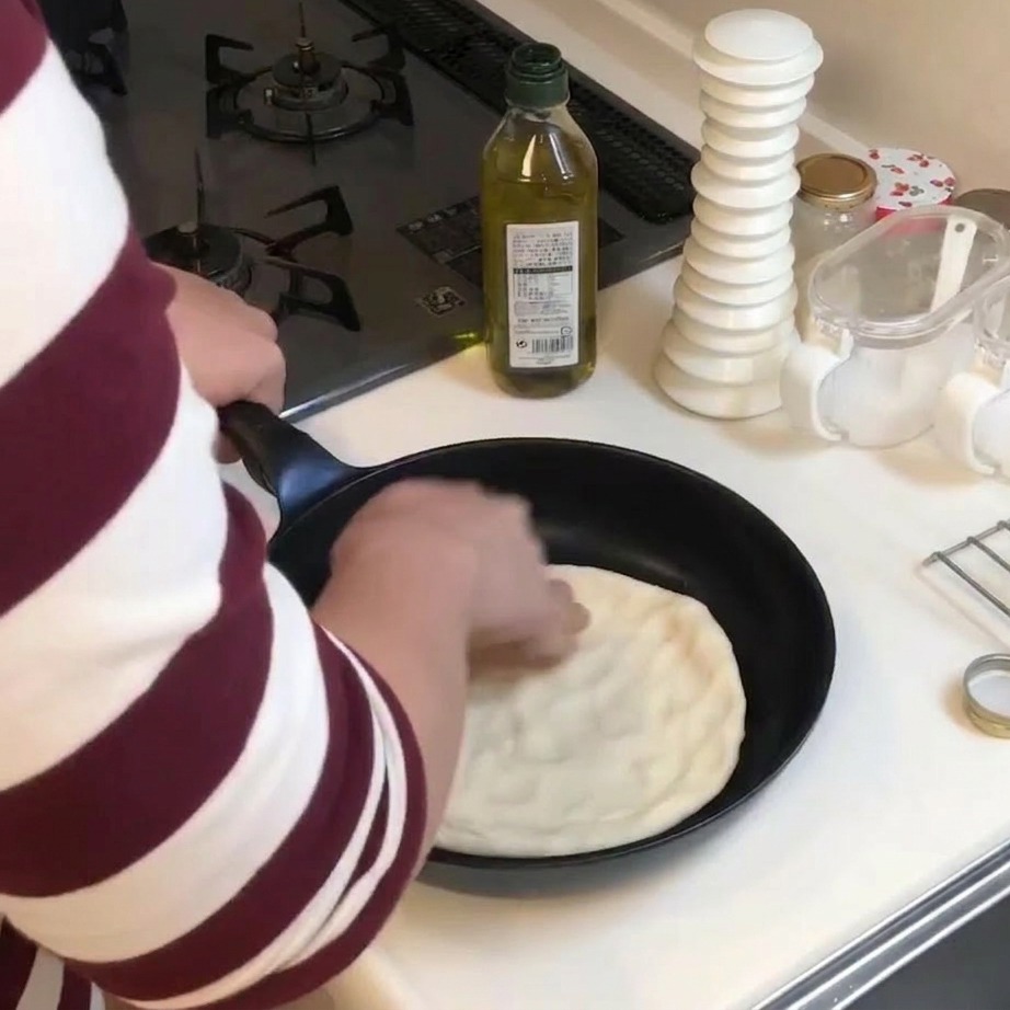 Una persona usa le mani per premere e appiattire un disco di pasta in una padella nera.