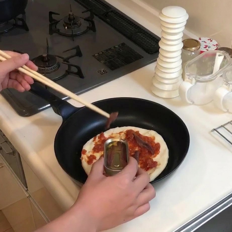 Uso di bacchette di legno per prelevare acciughe da una scatoletta e posizionarle sulla base della pizza condita.