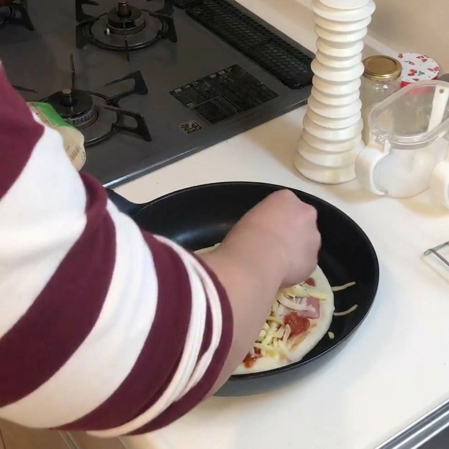 Una mano spruzza uno strato abbondante di formaggio grattugiato giallo e bianco su una pizza condita in padella.