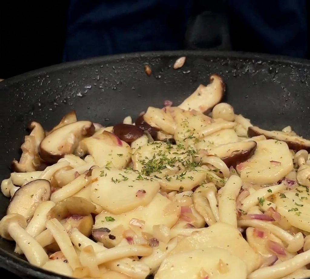 Del prezzemolo verde appena tritato viene spolverato su un mix di funghi e cipolle saltati in una padella nera.