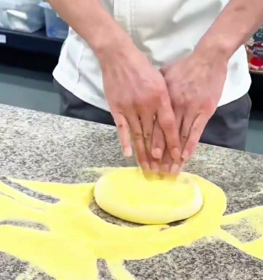 Mani che premono un panetto di impasto per pizza su un piano di marmo infarinato.