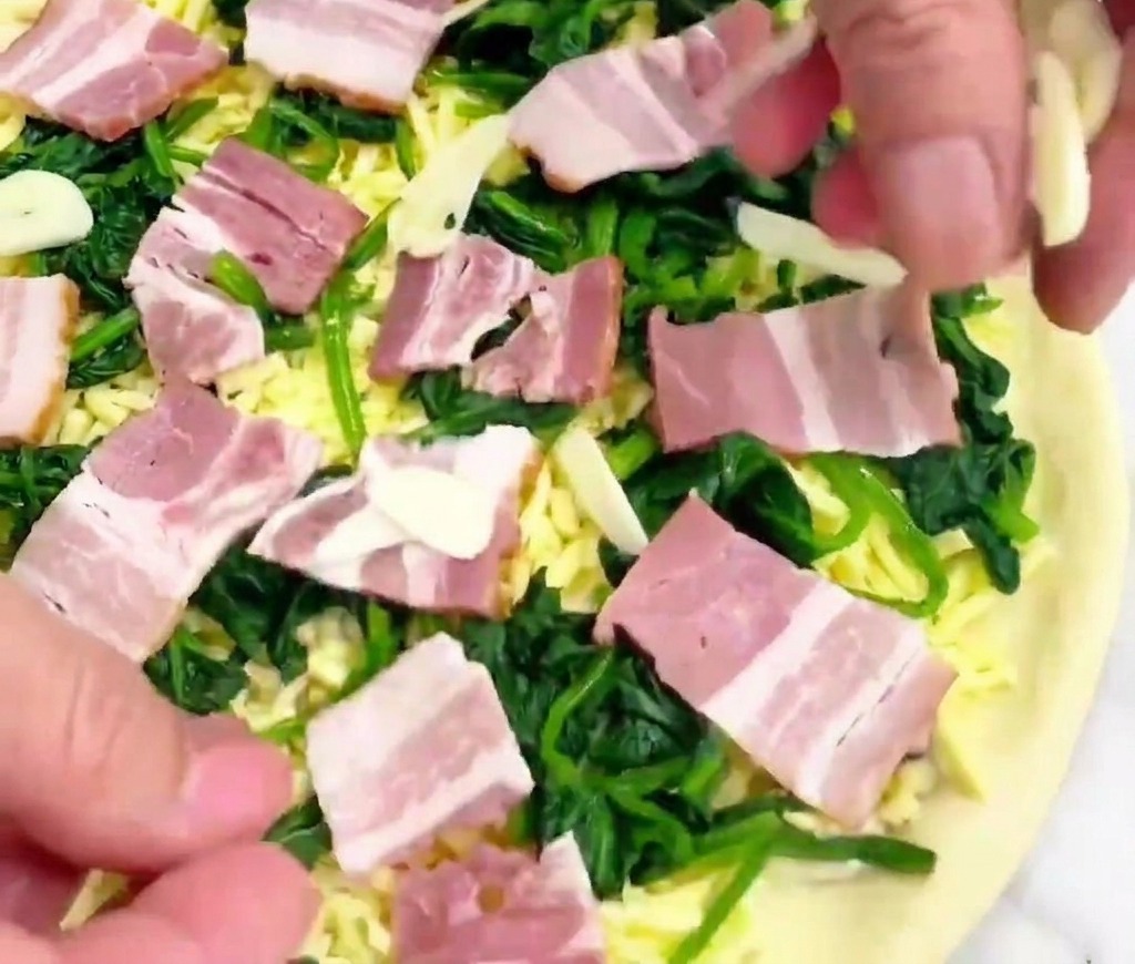 Mano che sparge fettine sottili di aglio su una pizza pronta per essere infornata.