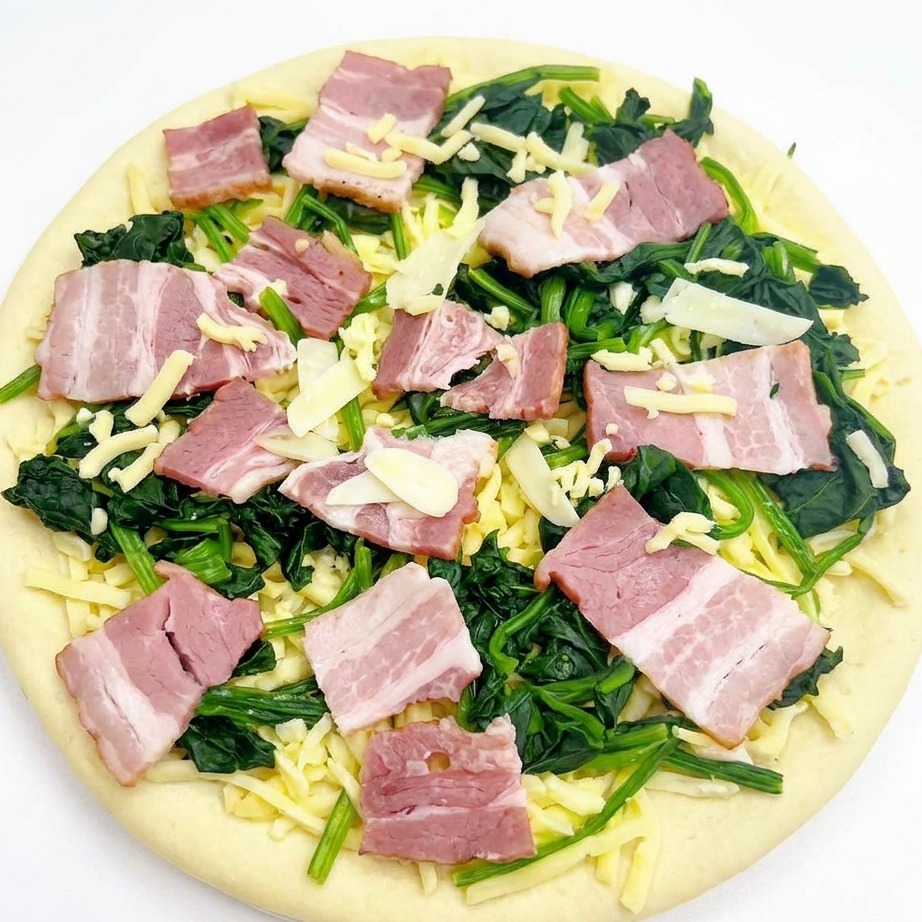 Pizza assemblata cruda con spinaci, pancetta e aglio, ricoperta da una leggera pioggia di mozzarella.