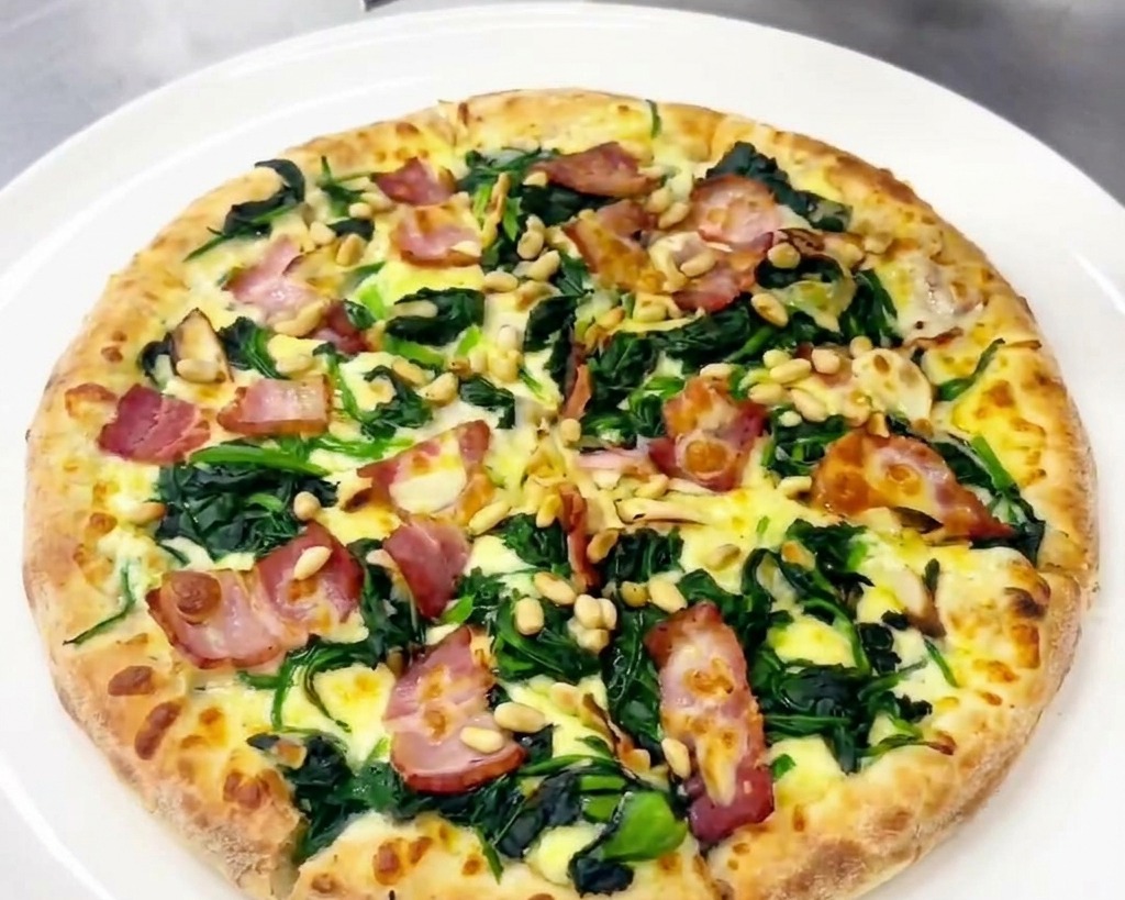Persona che usa un coltellino per aggiungere scaglie di formaggio stagionato sulla pizza guarnita.