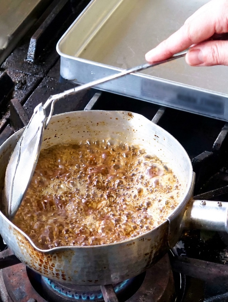 Fettine di aglio che friggono in un pentolino con olio che bolle vigorosamente e vapore che sale dalla superficie.