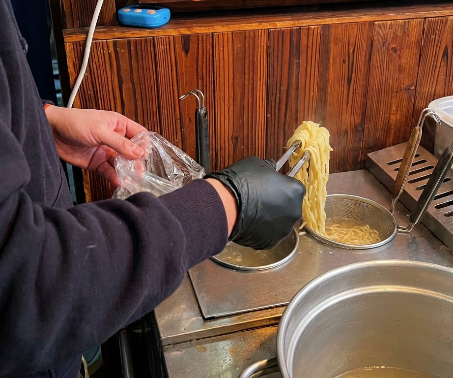 Noodle gialli per ramen sollevati con pinze da una pentola dacqua bollente per essere messi nella ciotola.