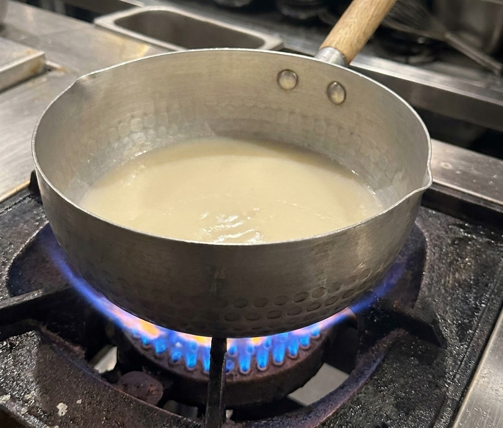 Primo piano di una pentola in metallo con brodo bianco e piccole gocce dolio che brillano in superficie.