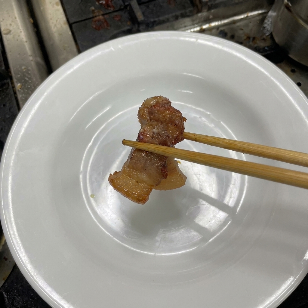 Bacchette che sollevano una fetta di pancetta scura e lucida.